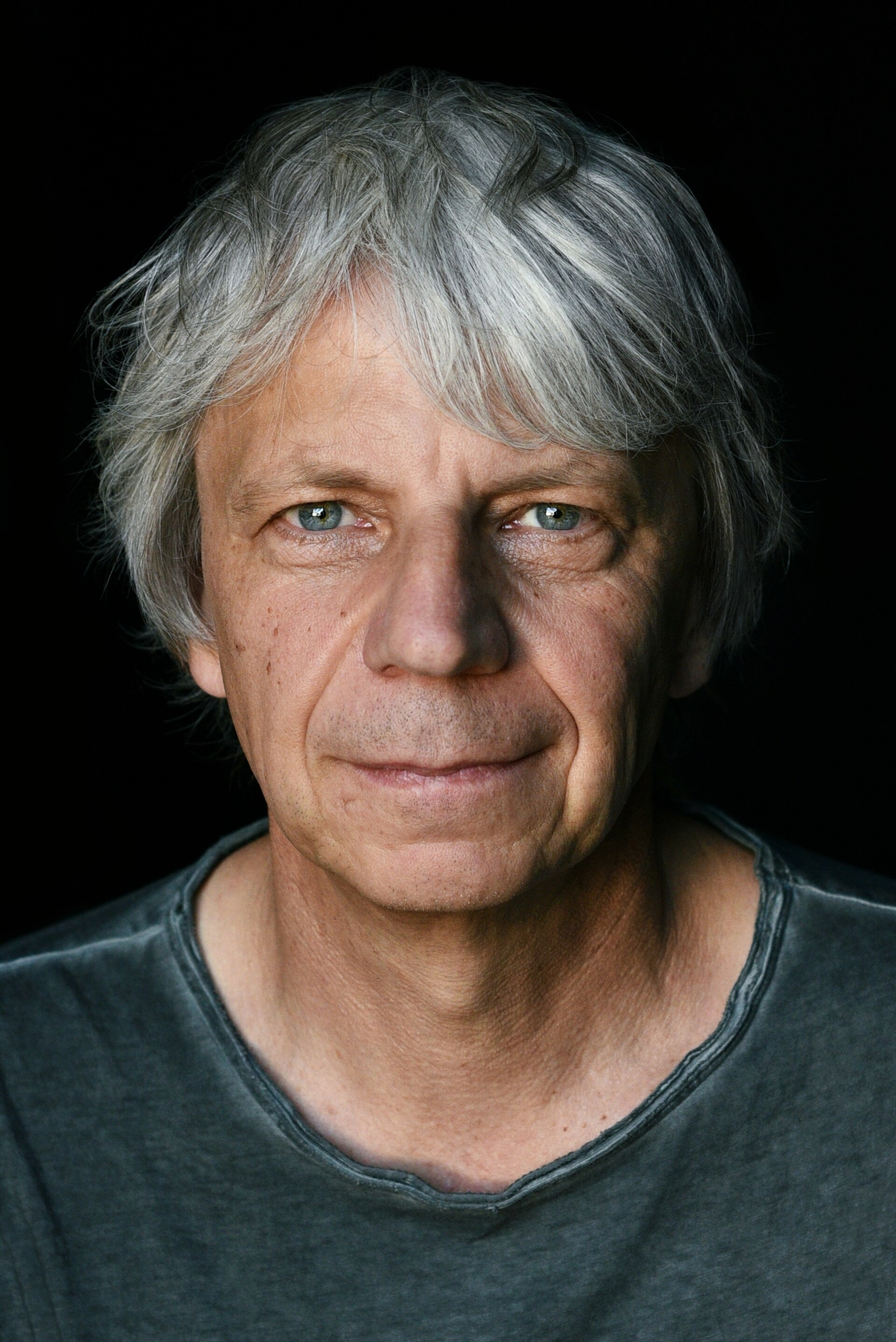 A portrait of 60-year-old German filmmaker Andreas Dresen, who has grey hair and blue eyes.