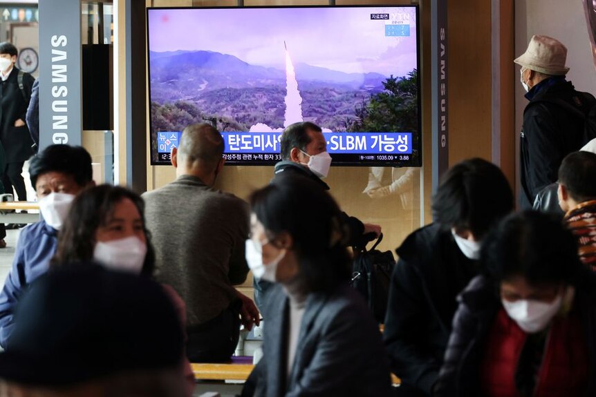 People watch a television screen showing the firing of a ballistic missile.
