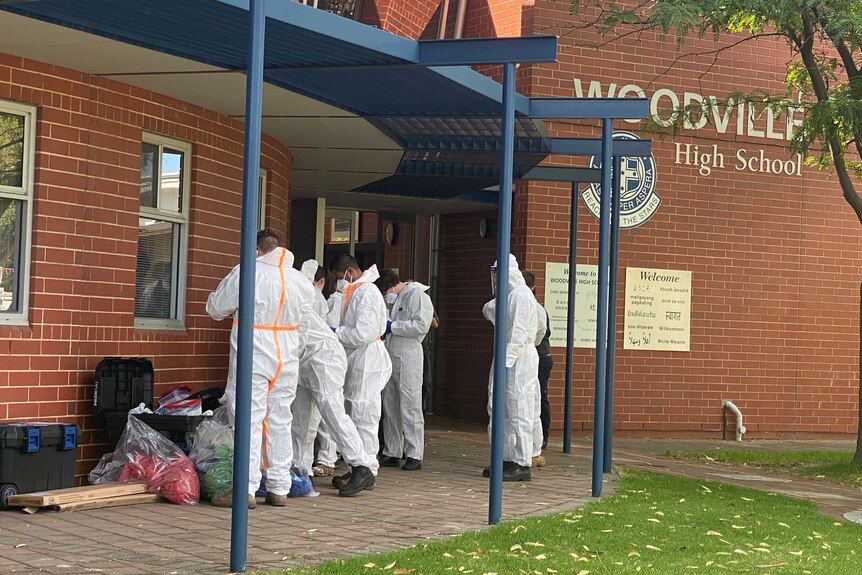 Several people dress in personal protective equipment in front of Woodville High School.