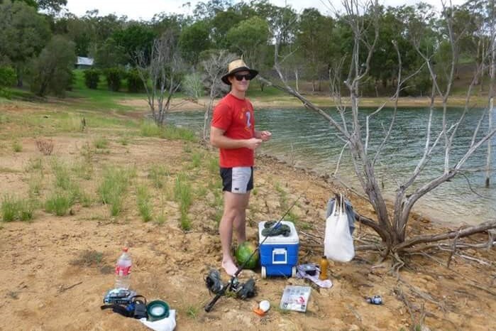 Calum McKinnon with his fishing gear surrounding him, standing by a body of water