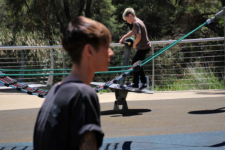 A wide shot showing a young boy standing on playground equipment with a woman in the foreground out of focus.