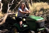 Shirley Hinkley sits on a ride-on mower on her property in Daylesford, that is surrounded by trees.