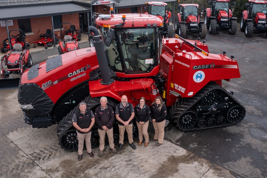 Five people standing in front of a giant red tractor 