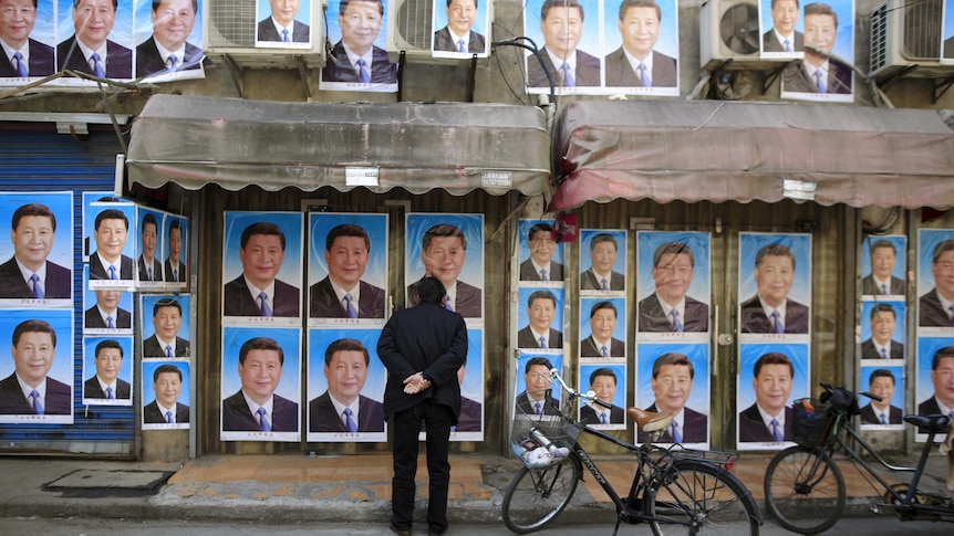 A man looks at a building covered in hundreds of posters of Chinese President Xi Jinping