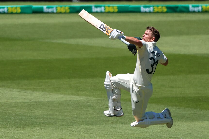David warner punches the air and leaps high with his bat pointing in front of him
