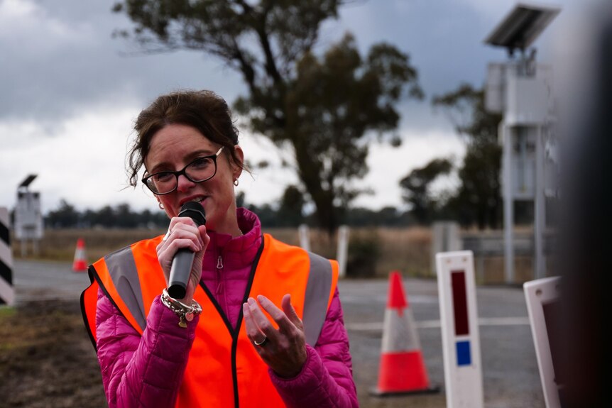 woman with microphone and high vis vest speaking at a railway crossing.