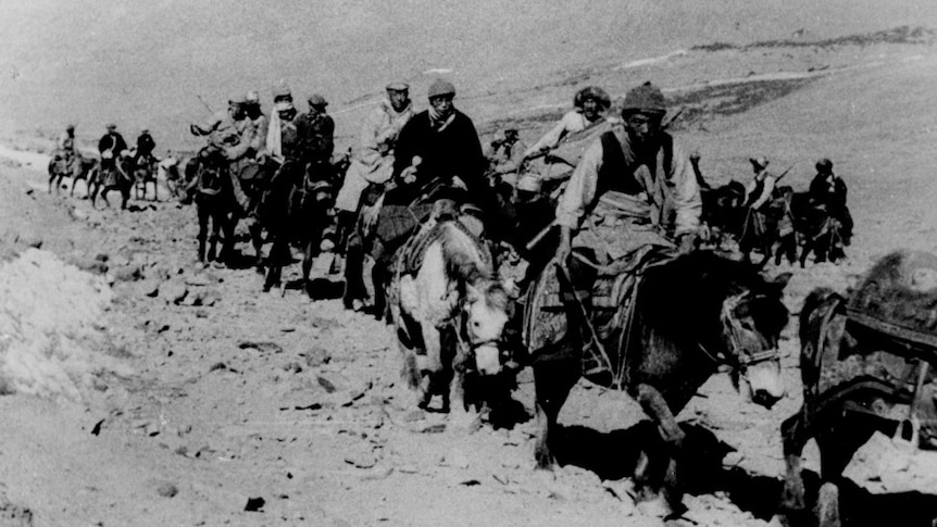 A group of men stand by as the Dalai Lama, in a scarf, glasses and hat, rides past