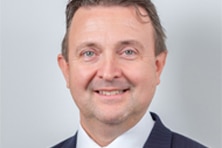 Headshot of a white middle aged man with blue eyes in a suit