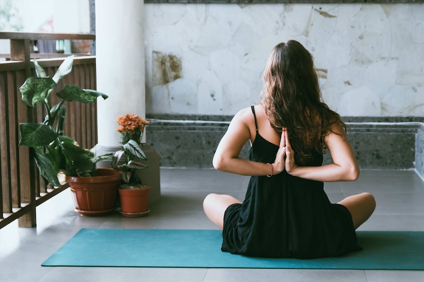 Woman doing yoga on a balcony for a story about the bare minimum amount of exercise you need to stay healthy.