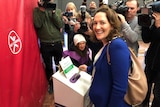 A woman laughs towards the camera as she votes, with media behind her.