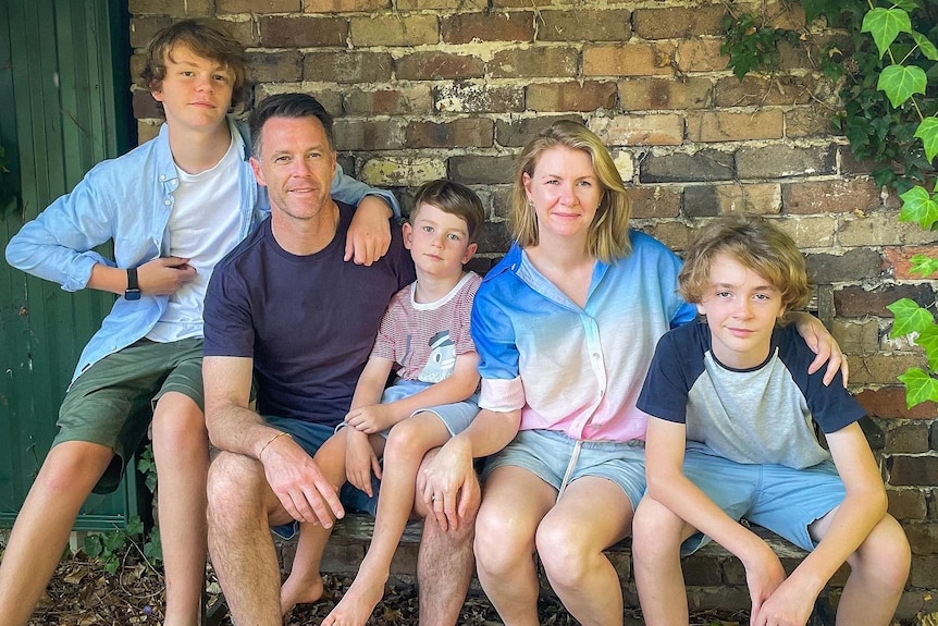 a man sitting on a  brick wall with his wife and three young boys