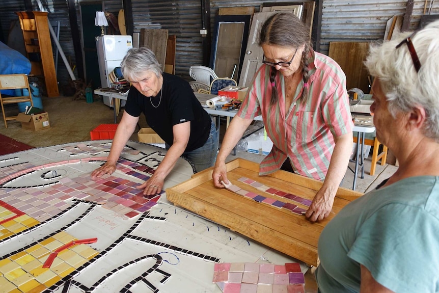 Three women arranging colourful tiles of a white board.