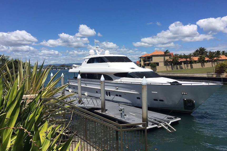 A luxury yacht is moored in the calm waters of a Gold Coast canal on a sunny day.