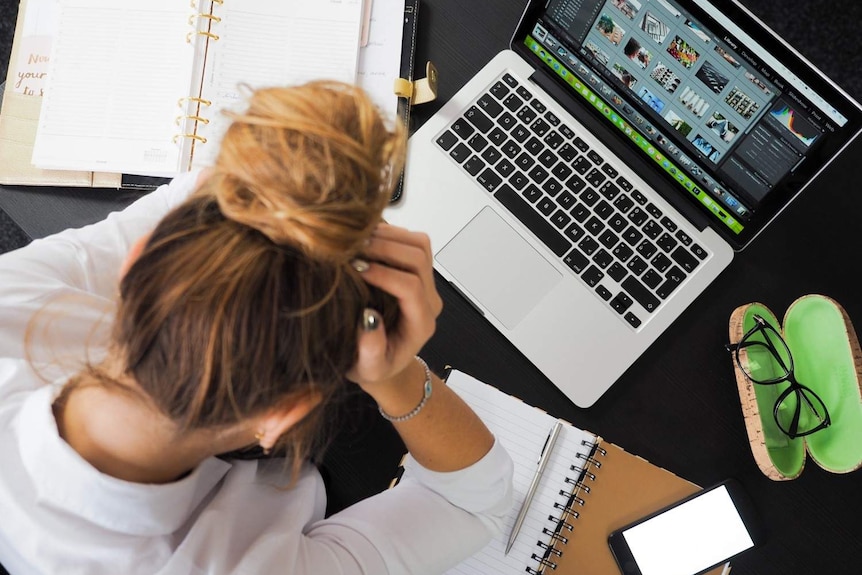 A young woman sits with her head in her hands at her desk.