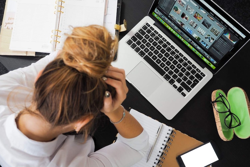 A young woman sits with her head in her hands at her desk.