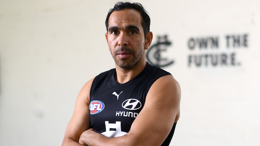 AFL player standing with his arms crossed in front of a sign  