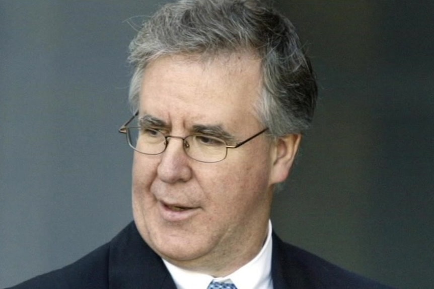 A close up of a man wearing glasses with wavy greying hair