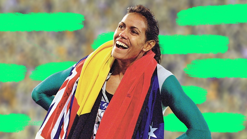 Cathy freeman smiles to the crowd with the Australian and Aboriginal flags draped over her.
