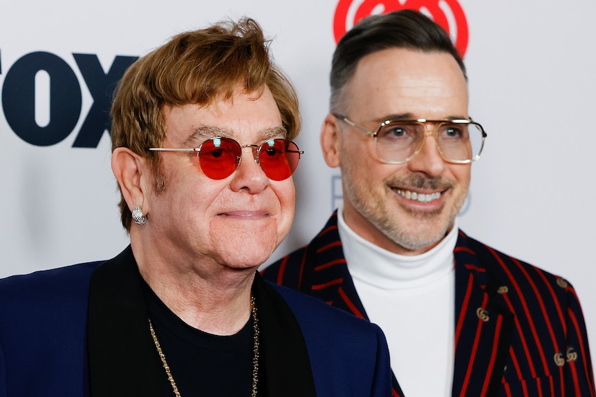 elton john and david furnish smile next to each other at a red carpet event