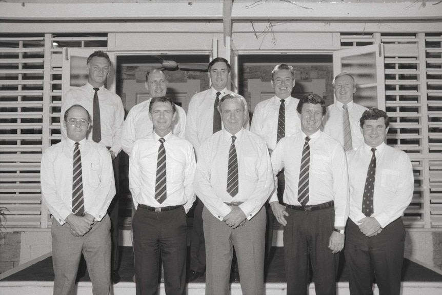 A black-and-white photo of nine male politicians standing out the front of a building.