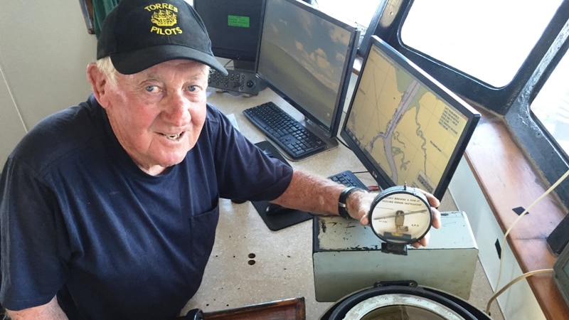 80-year-old master mariner holds a compass needle next to a ship's magnetic compass