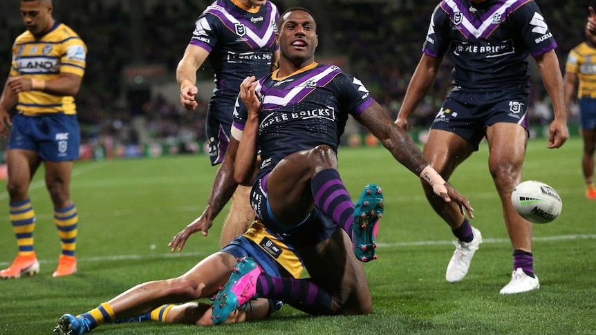 An NRL player poses in triumph after scoring a try in finals, as his teammates celebrate behind him.