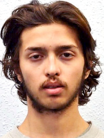 A mugshot of a young man with wavy brown hair and light facial hair.