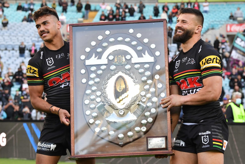 Two Penrith Panthers NRL players stand with the JJ Giltinan Shield after beating Canterbury.