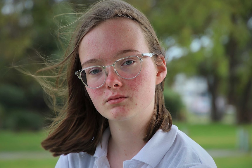 A headshot of a teenage girl with glasses wearing a white school uniform polo shirt.
