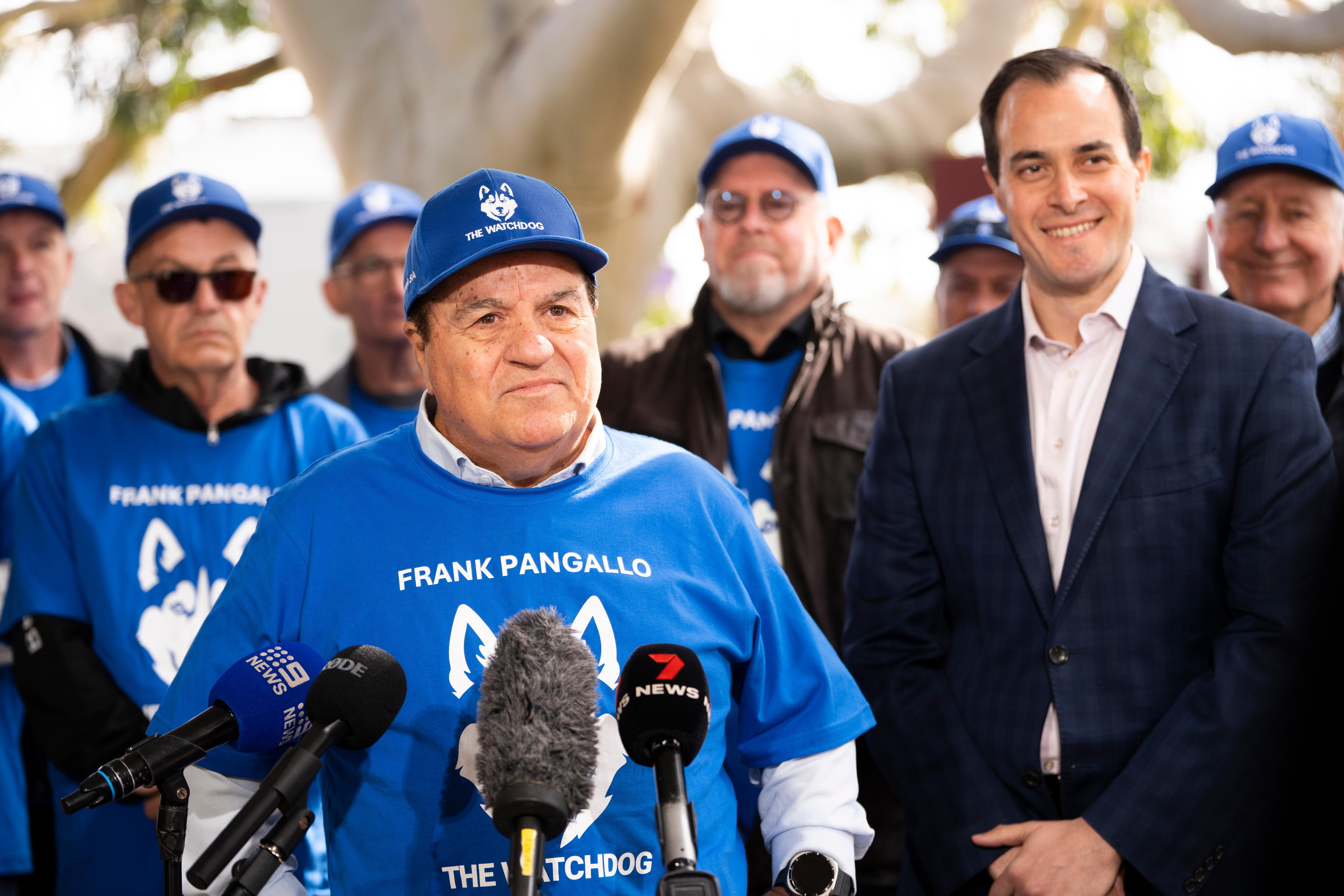 Frank Pangello con camiseta azul y gorra junto a Vincent Tarzia en una conferencia de prensa política.