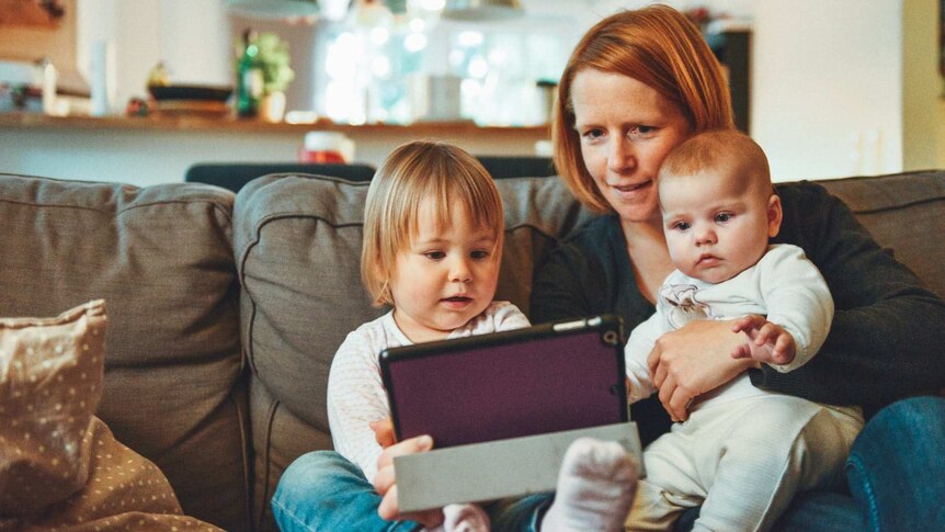 A mother on a couch with two young children looking at an iPad