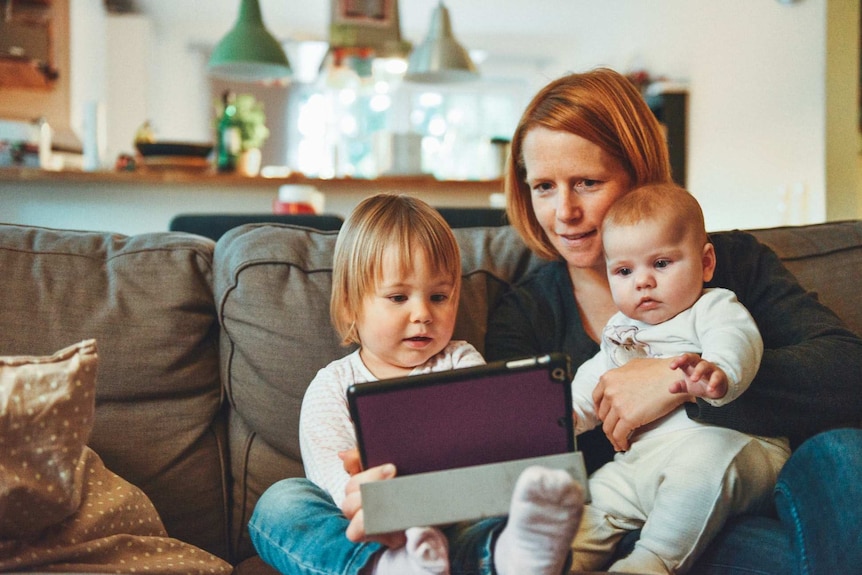 A mother on a couch with two young children looking at an iPad