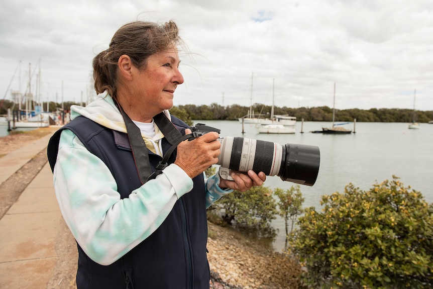 A woman on a shore holds a camera ready to photograph