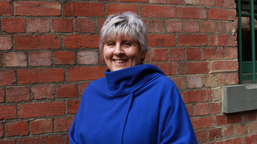 Carmen Barnsley stands in front of a red brick wall smiling.