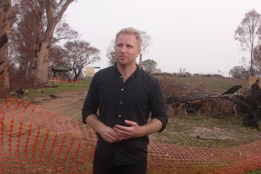 Macdonald standing in front of burnt area roped off by orange plastic temporary net fence.