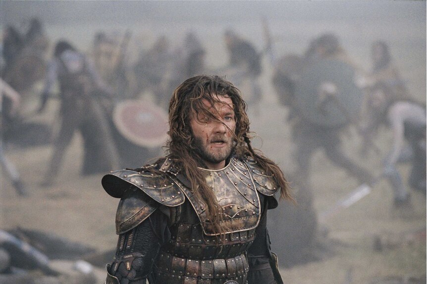A movie still of Joel Edgerton with long hair and wearing armour in the movie King Arthur