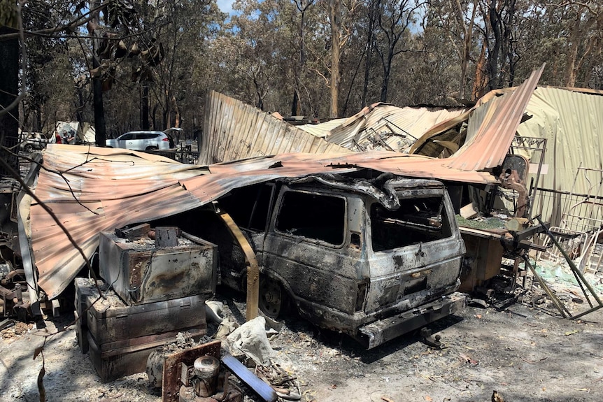 A burnt out car beneath a collapsed, smouldering shed in Cooroibah