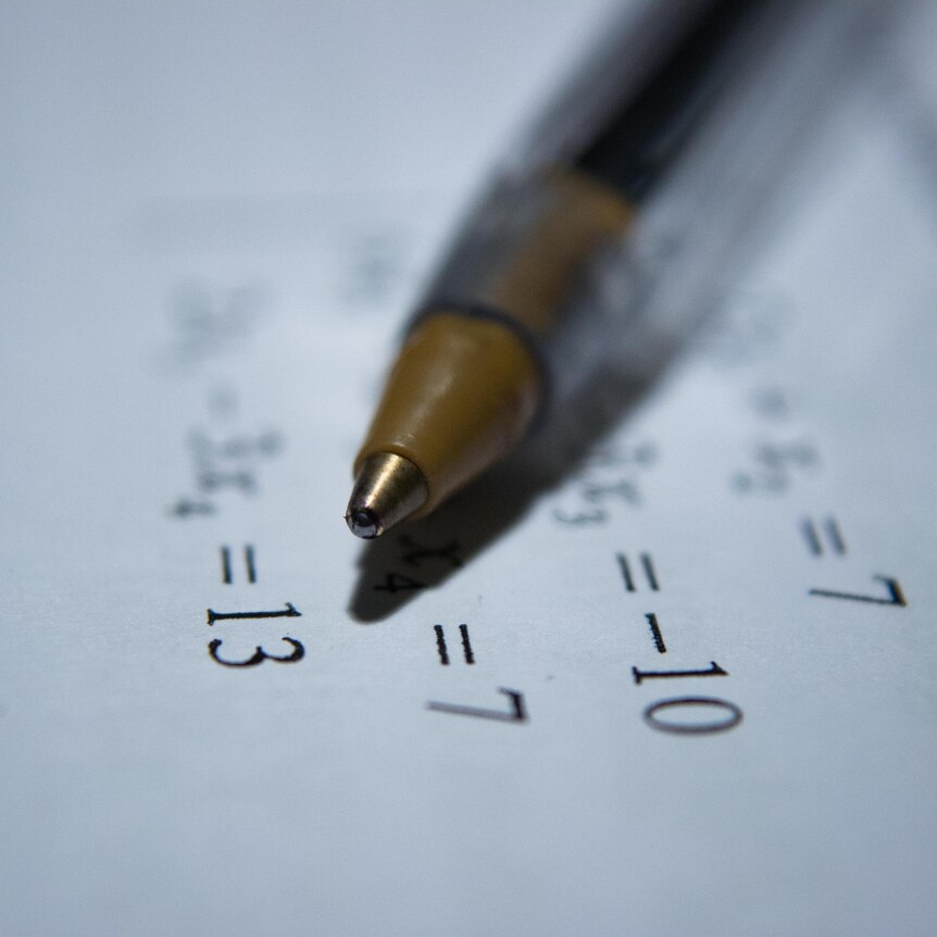 A close up shot of a pen on a piece of paper printed with a maths equation.