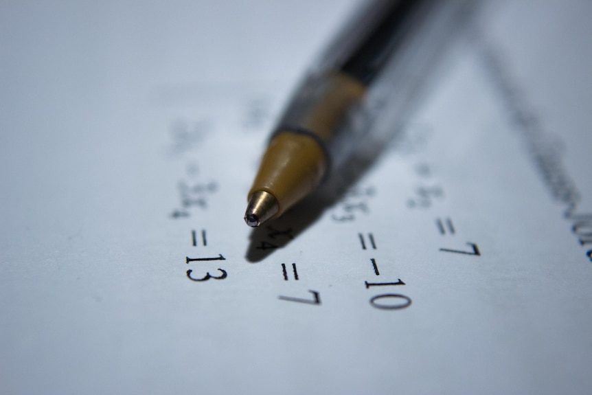 A close up shot of a pen on a piece of paper printed with a maths equation.