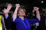 Looking up at a crowd of people surrounding Nicola Sturgeon with their hands in the air.