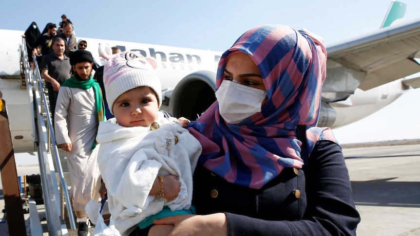 A woman in a hijab and face mask clutches her baby
