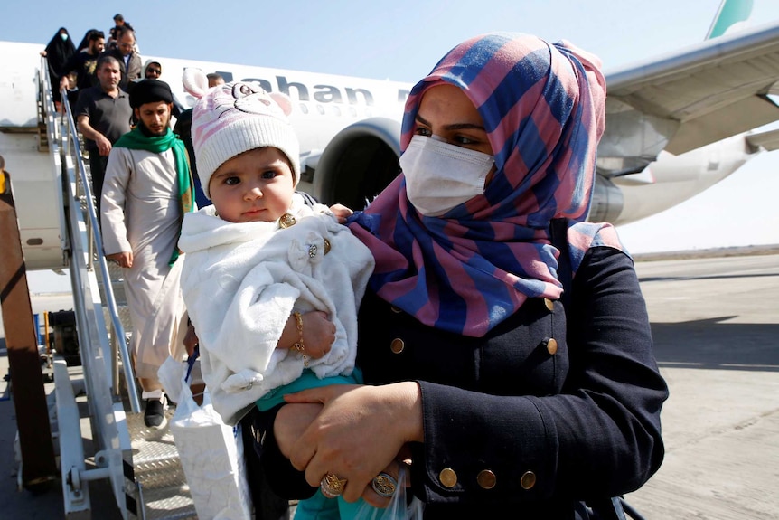 A woman in a hijab and face mask clutches her baby