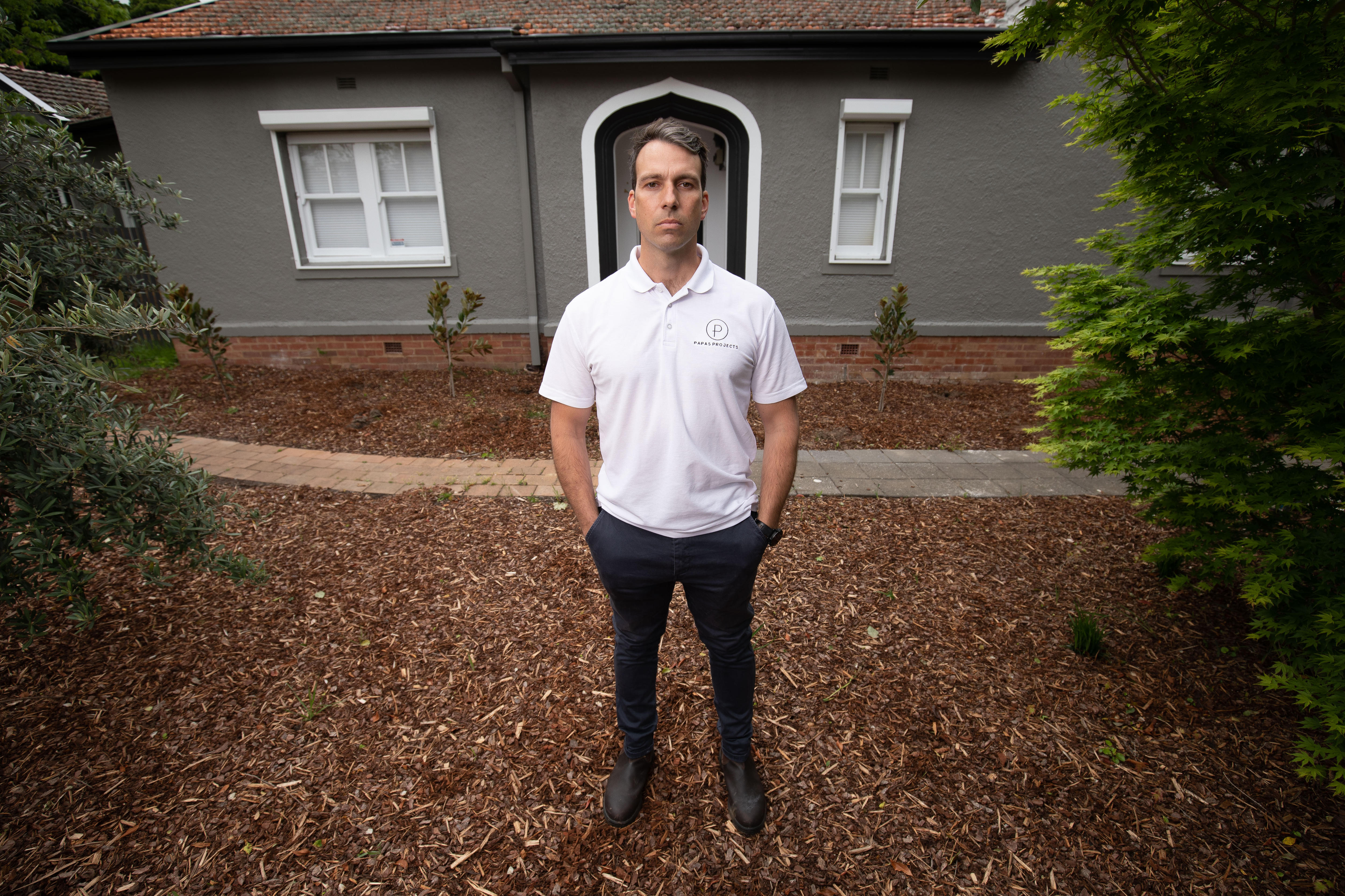 A man stands outside a house. He looks serious.