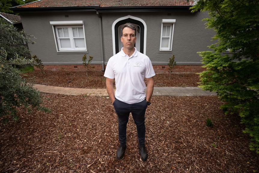 A man stands outside a house. He looks serious.