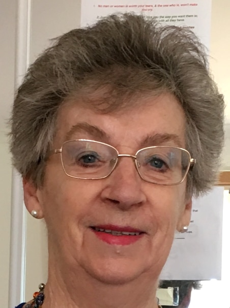 A grey-haired woman with glasses smiles at the camera
