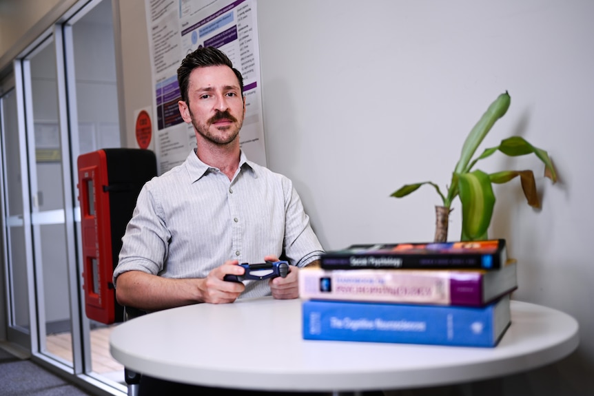 A man with a video game controller next to a pile of books