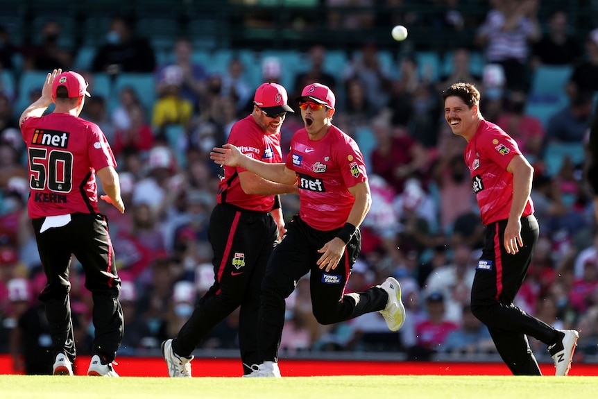 Sean Abbott (centre) looks amazed as Sydney Sixers teammates run around him and the ball hovers in the air.