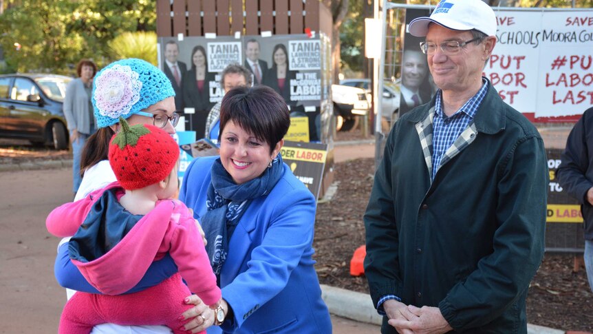Alyssa Hayden smiles and greets a baby being carried by a woman at a polling booth as Mike Nahan looks on.