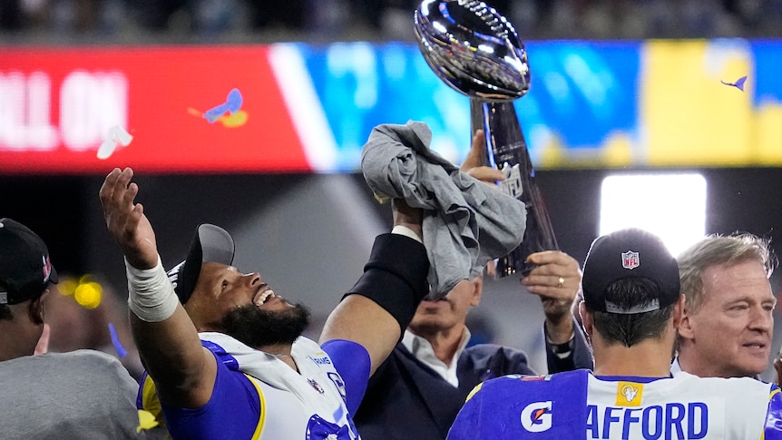 An NFL player raises his arms in the air in triumph as he stands next to the Vince Lombardi Trophy after Super Bowl LVI. 