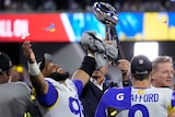 An NFL player raises his arms in the air in triumph as he stands next to the Vince Lombardi Trophy after Super Bowl LVI. 